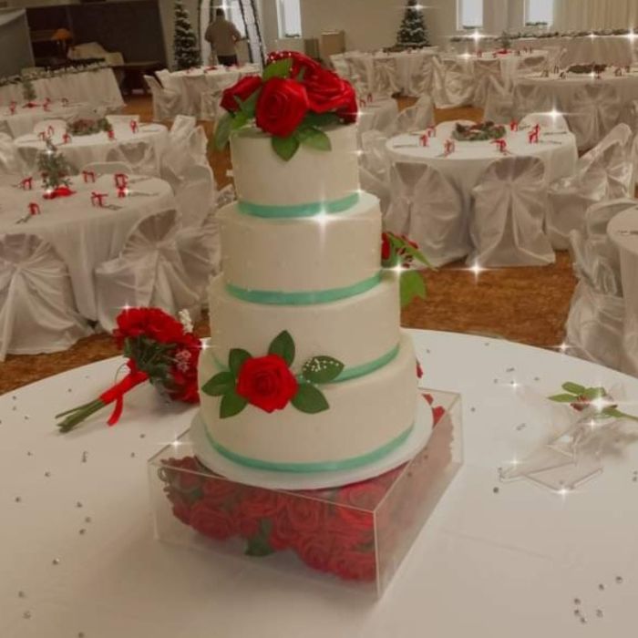 A four-tiered white wedding cake decorated with teal ribbons and fresh red roses at a wedding reception in Sharon, PA.
