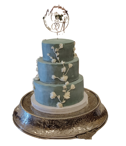 A three-tiered light blue wedding cake with white buttercream floral vine decorations and a gold topper by Sweet Sensations in Sharon, PA.